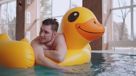 happy-man-in-water-park-lying-on-inflatable-duck-in-swimming-pool-joyful-and-relaxed-male-visitor